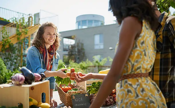 Female gardener selling organic crops and picking up a bountiful basket full of fresh produce