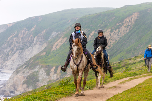 Point Reyes, California, USA - April 2, 2016:  Two people riding the horses and enjoying the weekend at Tomales Point of Point Reyes National Seashore, California. hiker on the background.