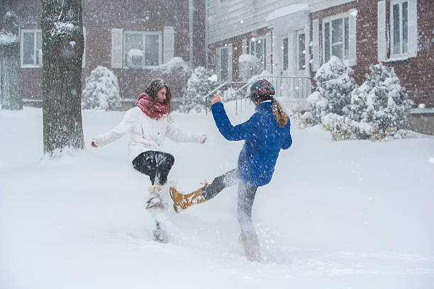 zwei teenager-mädchen spielt unter schneefall auf der straße - queens head stock-fotos und bilder