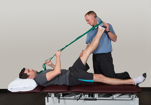 Physical therapist stretching patient's hamstring and leg with use of a stretching strap.