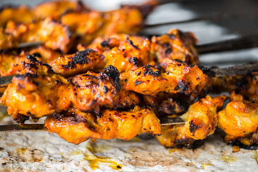 iStockalypse Dubai.  Closeup of freshly grilled chicken tikka masala kebabs on skewers dripping onto a piece of naan flatbread cooked in a Tandoori oven.  Dubai, UAE, Middle East, GCC.