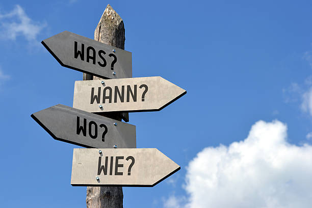 Questions signpost - in German Wooden singpost with "was? wann? wo? wie?" arrows against blue sky. info sign stock pictures, royalty-free photos & images