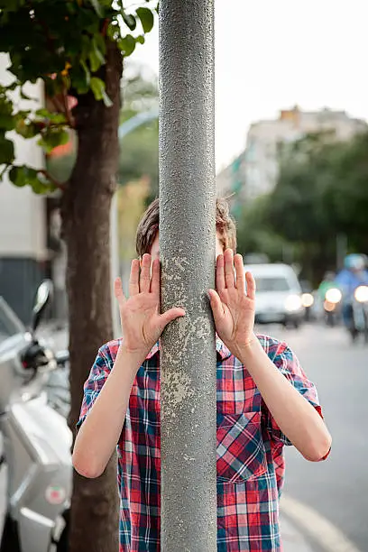 boy with hands up behind a lamppost