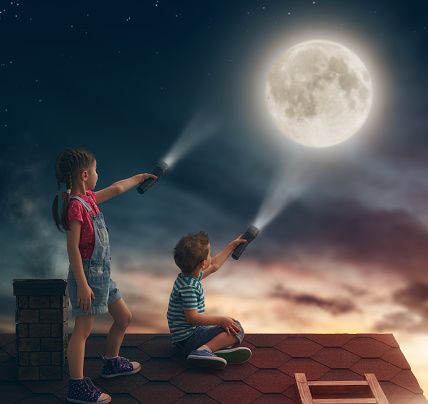 Two cute children sit on the roof and look at the moon.