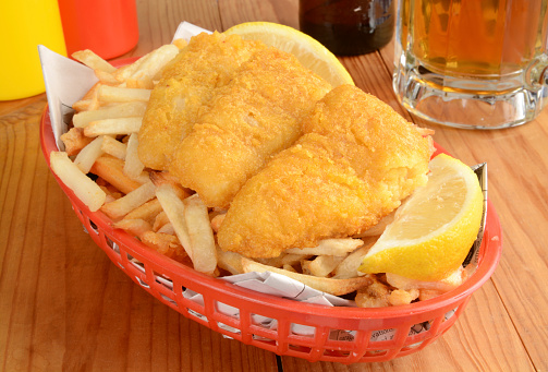 Fish and chips served in a basket wrapped in newsprint with a mug of beer