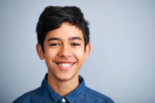 A cute young preteen boy standing and smiling against a grey background
