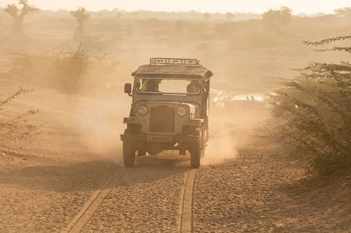 Jodhpur, India - December 4, 2015: Very popular in India off-road jeep Mahindra driving on safari down dusty country road near Bishnoi village, Jodhpur, Rajasthan, India  