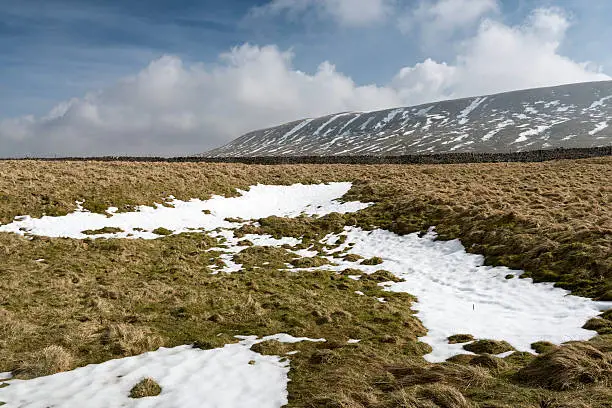 Early spring snow in a scenic view from Hem Gill Shaw towards Little Whernside in the hills above Kettlewell in the Yorkshire Dales. 