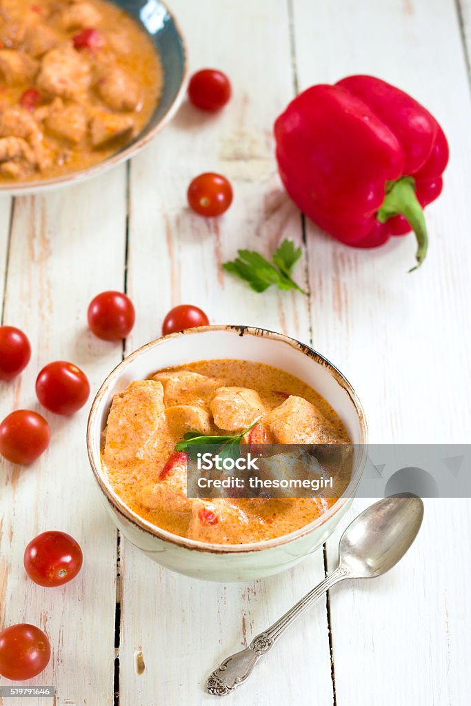 Delicious chicken stew with paprika in a bowl Delicious chicken stew with paprika in a bowl on a white wooden table. With fresh cherry tomatoes, red bell pepper and parsley. Traditional hungarian dish paprikash. Comfort food. Selective focus Appetizer Stock Photo