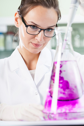 Female scientist putting violet liquid into the flask