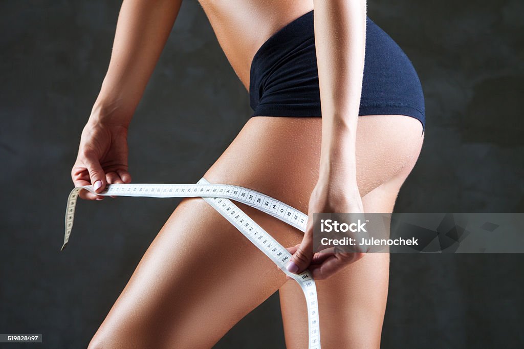Slimming woman measuring thigh with tape slimming woman measuring her thigh with measuring tape over dark gray background Adult Stock Photo