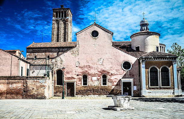 The faded red Church of San Giacomo dell'Orio in Venice, Italy with the Bell Tower and medieval well.