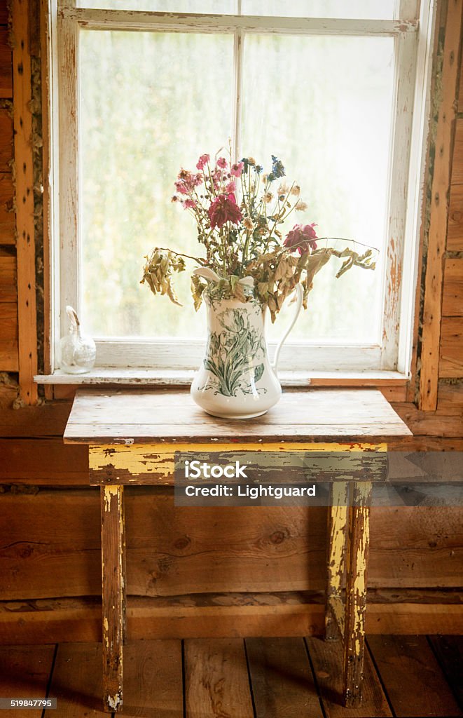 Rustic cabin dried flowers vase of flowers grace antique table in front of cabin window Antique Stock Photo