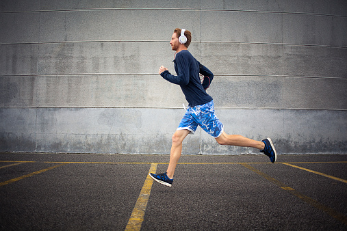 Young fit man running and listening to music in an urban environment. Shallow DOF. Developed from RAW; retouched with special care and attention; Small amount of grain added for best final impression; Ready made for print and web use;