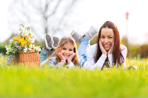 Mother and daughter lying on grass in park, looking at camera and smiling