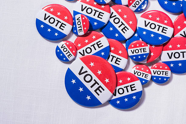 istock Various size Patriotic VOTE buttons on white table cloth 519864216