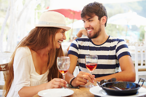 Young Couple Enjoying Meal In Outdoor Restaurant Smiling And Laughing