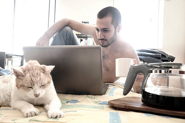 Man using laptop on his bed while drinking coffee stock photo
