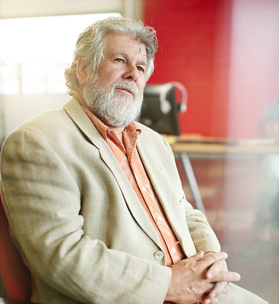 Casual portrait of a mature business man using technology in a bright and sunny startup with windows in the background