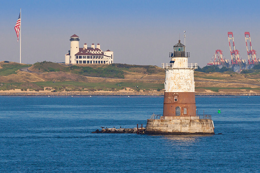 Robbins Reef Light, with Bayonne Golf Club and Cranes of Port Bayonne in background, Bayonne, NJ, USA. The image lit by early morning sun. The Robbins Reef Light Station is a sparkplug lighthouse located off Constable Hook in Bayonne, along the west side of Main Channel, Upper New York Bay. The tower and integral keepers quarters were built in 1883.