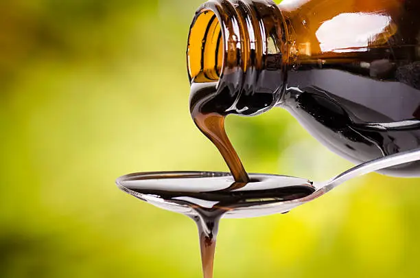 Photo of pouring a liquid on a spoon. Natural green background.