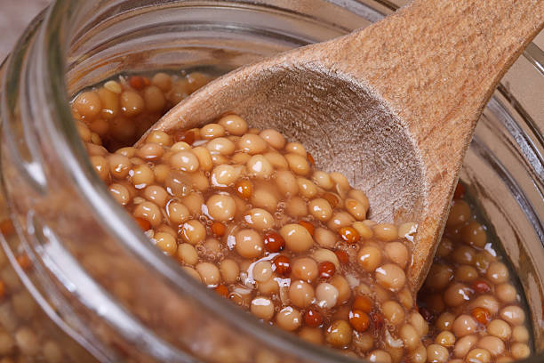 Dijon mustard on a wooden spoon Dijon mustard on a wooden spoon in a glass jar closeup. macro dijonnaise stock pictures, royalty-free photos & images