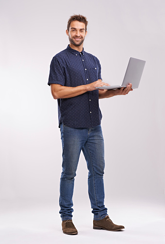 Full length studio shot of a handsome man holding a laptop