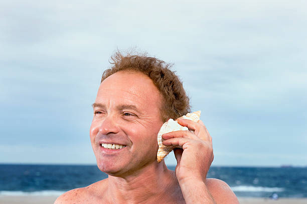 istock Mature man holding shell up to ear, smiling, close-up 519888963