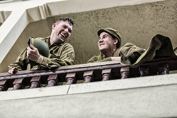 Two World War II US Army soldiers taking a break - bantering and laughing as they relax together - leaning over the railing of an upstairs balcony at a dance hall.