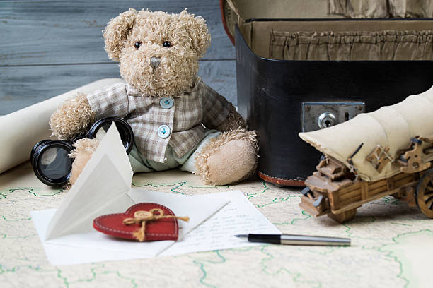 Travel concept, teddy bear with old binoculars and suitcase on the antique map with letter and a fountain pen