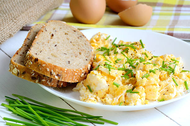 Scrambled eggs with wholemeal bread and fresh chives on white wooden table