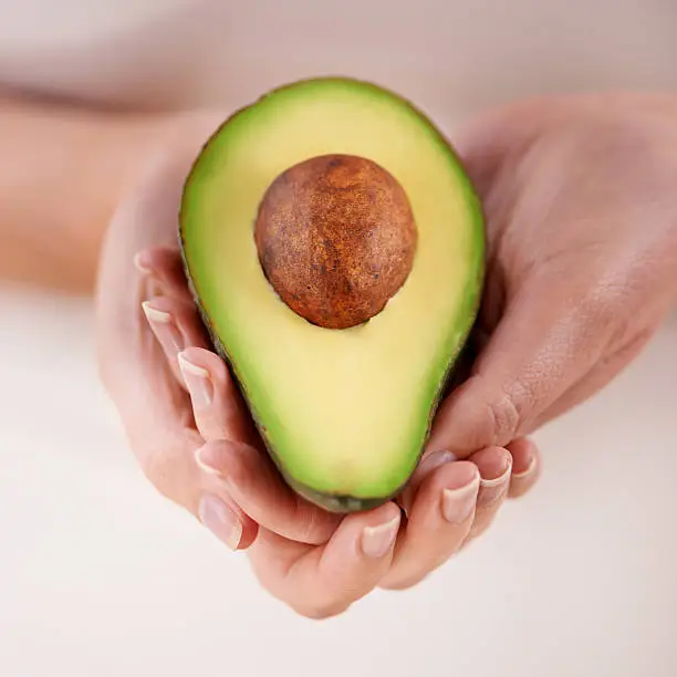 Cropped shot of a woman holding half of an avocado in her hands