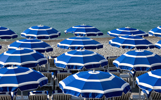 Beach with blue umbrellas near Promenade des Anglais in city of Nice, France.