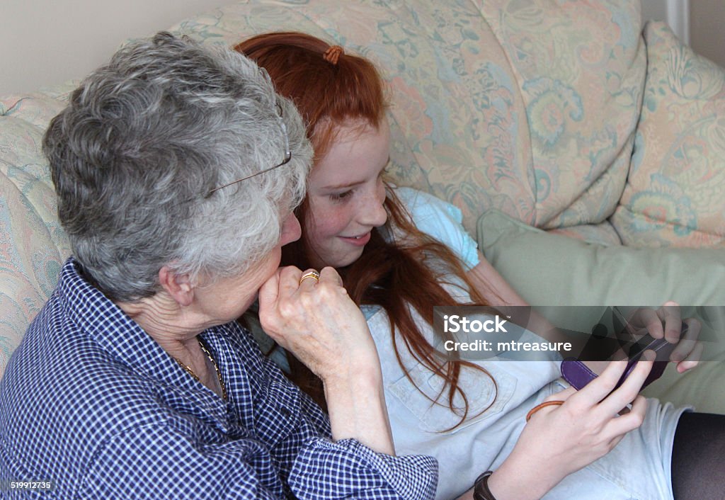 Girl showing grandmother how to use mobile phone / smartphone image Photo of a young girl showing her grandmother how to use a mobile phone computer / smartphone.  They are pictured sat on the sofa together, laughing and smiling as they look at something funny and share the joke. Active Seniors Stock Photo