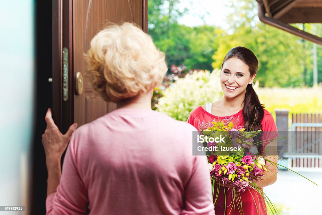 Young woman bringing birthday flowers to her grandmother Happy young woman bringing birthday flowers to senior woman, standing at the entrance door and smiling.  Gift Stock Photo
