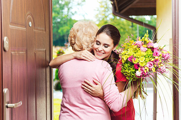 Young woman bringing birthday flowers to her grandmother Happy young woman bringing birthday flowers to senior woman, standing at the entrance door and hugging.  birthday wishes for daughter stock pictures, royalty-free photos & images