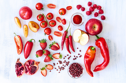 Collection of fresh red toned vegetables and fruits raw produce on white rustic background, peppers capsicum chilli strawberry raspberry pomegranate tomato paprika azuki beans plum