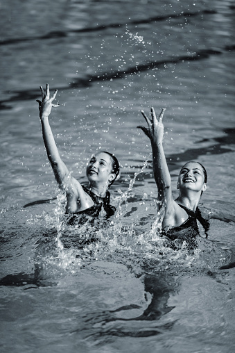Synchronized swimmers duet performing their routine. Toned black and white photo