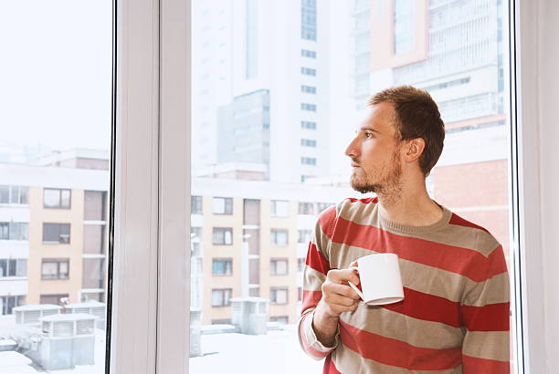 istock Young man drinking coffee and looking through the window 519927910