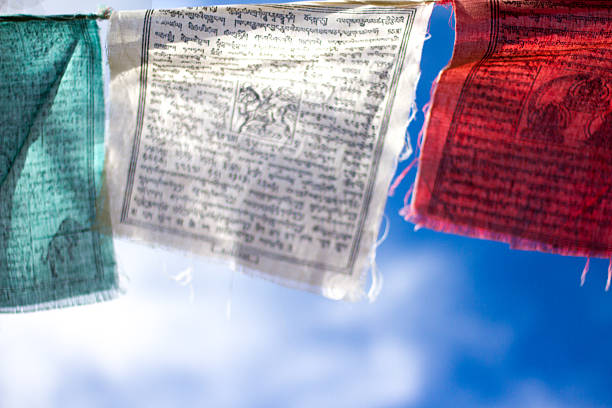 Colorful (green, white, red) Tibetan Buddhist prayer flags fluttering against a cloudy blue sky (close-up).