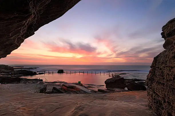 Sensational sunrise at Mahon rock pool, Maroubra, bathing the rocks and pool in vibrant reds and pink hues while a cave adds some interesting textures and framing to the scene.