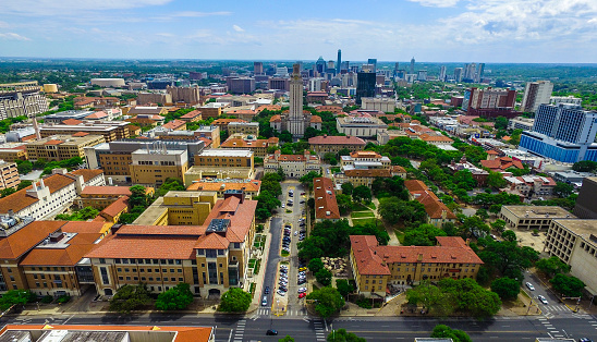 UT Tower Aerial over Campus University of Texas Austin aerial scene with the Austin Texas skyline citscape in the background taken from an aerial drone this amazing nature coverd capital city is a gorgeous sight on a nice spring day like this one. The High UT Main Building the Sniper Tower of the historic Shooting 