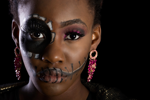 Horizontal studio shot on black of young black woman in black and white Day of the Dead makeup. Horizontal closeup with copyspace.