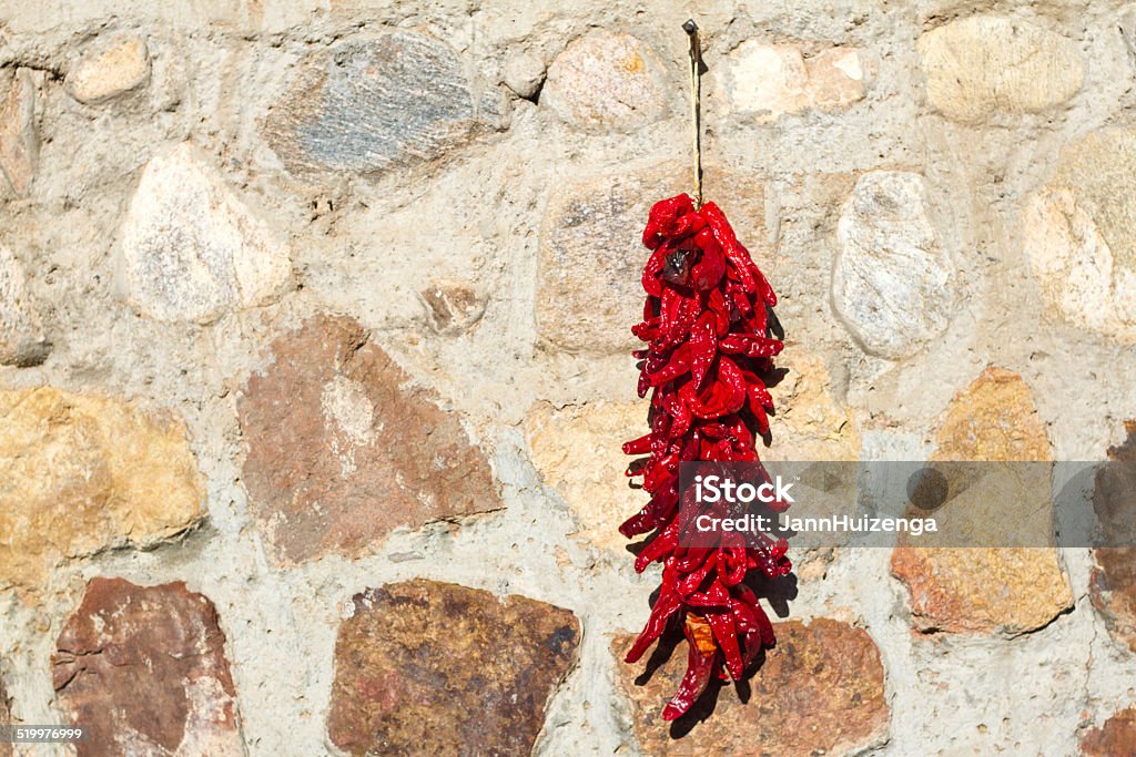 Red Chili Pepper Ristra Hangs On Stone Wall, New Mexico A red chili pepper ristra hanging on a stone wall in New Mexico. (A ristra hung on a house in NM is not only decorative, but it also protects from evil spirits, according to traditional beliefs.) Chili Pepper Stock Photo
