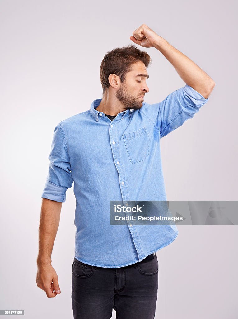 Deodorant needed Studio shot of a handsome young man smelling his sweat-soaked armpits against a gray background Sweat Stock Photo