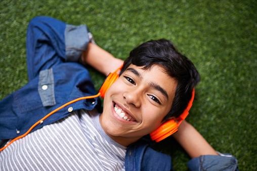 A young boy relaxing on the lawn and listening to music