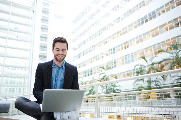 uomo sorridente utilizzando un computer portatile - office indoors contemporary office building foto e immagini stock