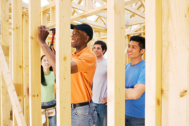 Group watching carpenter hammering nails into wooden house construction
