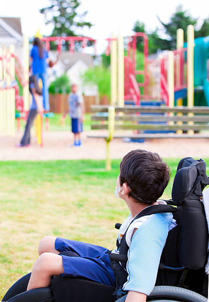 маленький мальчик с ограниченными возможностями в инвалидном кресле за просмотром дети играют на игровой площадке - ostracized стоковые фото и изображения