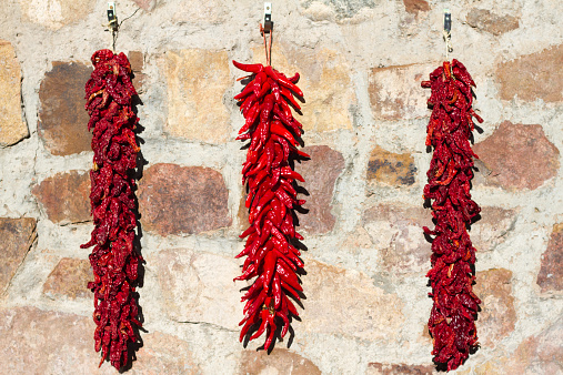 Three long red chili pepper ristras hang on a stone wall in New Mexico. (A ristra hung on a NM house is not only decorative, but it also protects from evil spirits according to traditional beliefs.)